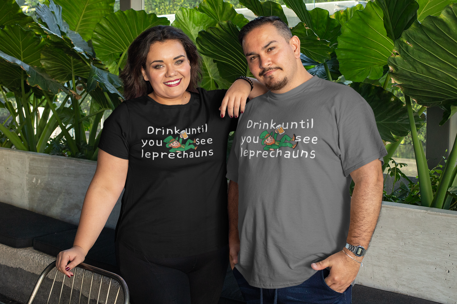 Middle aged Hispanic man and Hispanic woman standing outside near a beautiful garden wearing funny St Patrick's Day Drink Until You See Leprechauns. The woman is wearing a black t-shirt. The man is wearing a gray t-shirt in West Palm Beach, FL.